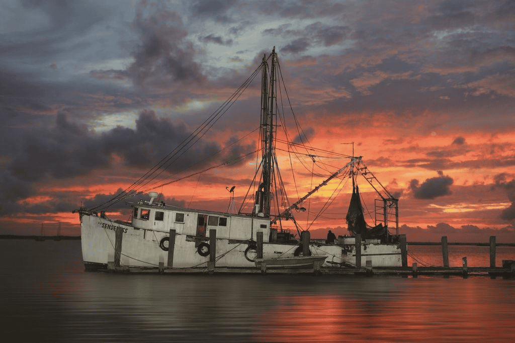 shrimp boat with View of downtown Fernandina Beach’s Centre Street at sunset, with brick storefronts, palm trees, and vintage streetlamps glowing.