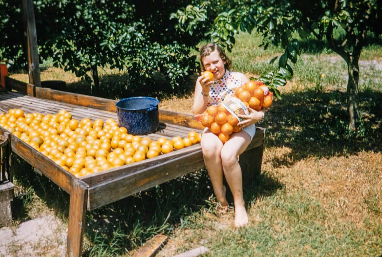 a woman sitting on a bench with a box of oranges